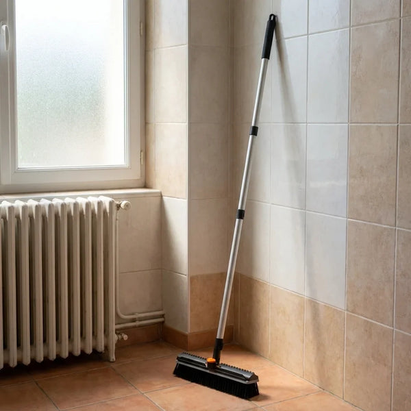 Une brosse à manche long rangée contre le mur de la salle de bain.
