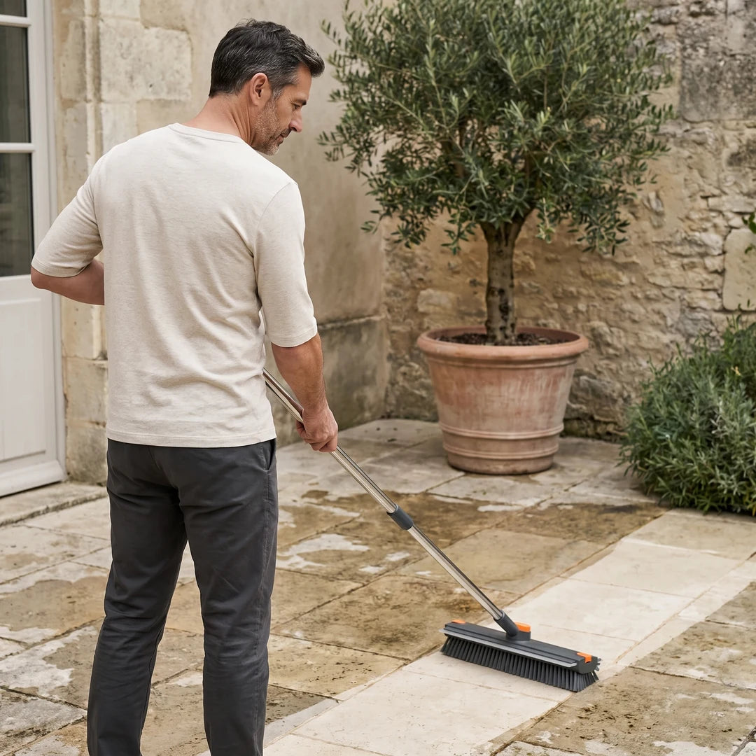 Homme de la cinquantaine nettoyant debout les dalles de sa terrasse avec la brosse NETTARIA, manche déployé